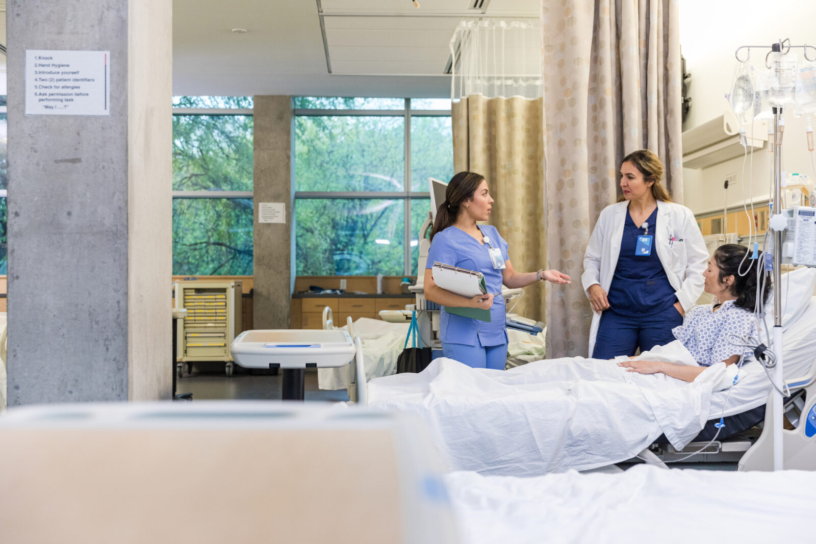 two people standing and speaking to a patient in a bed
