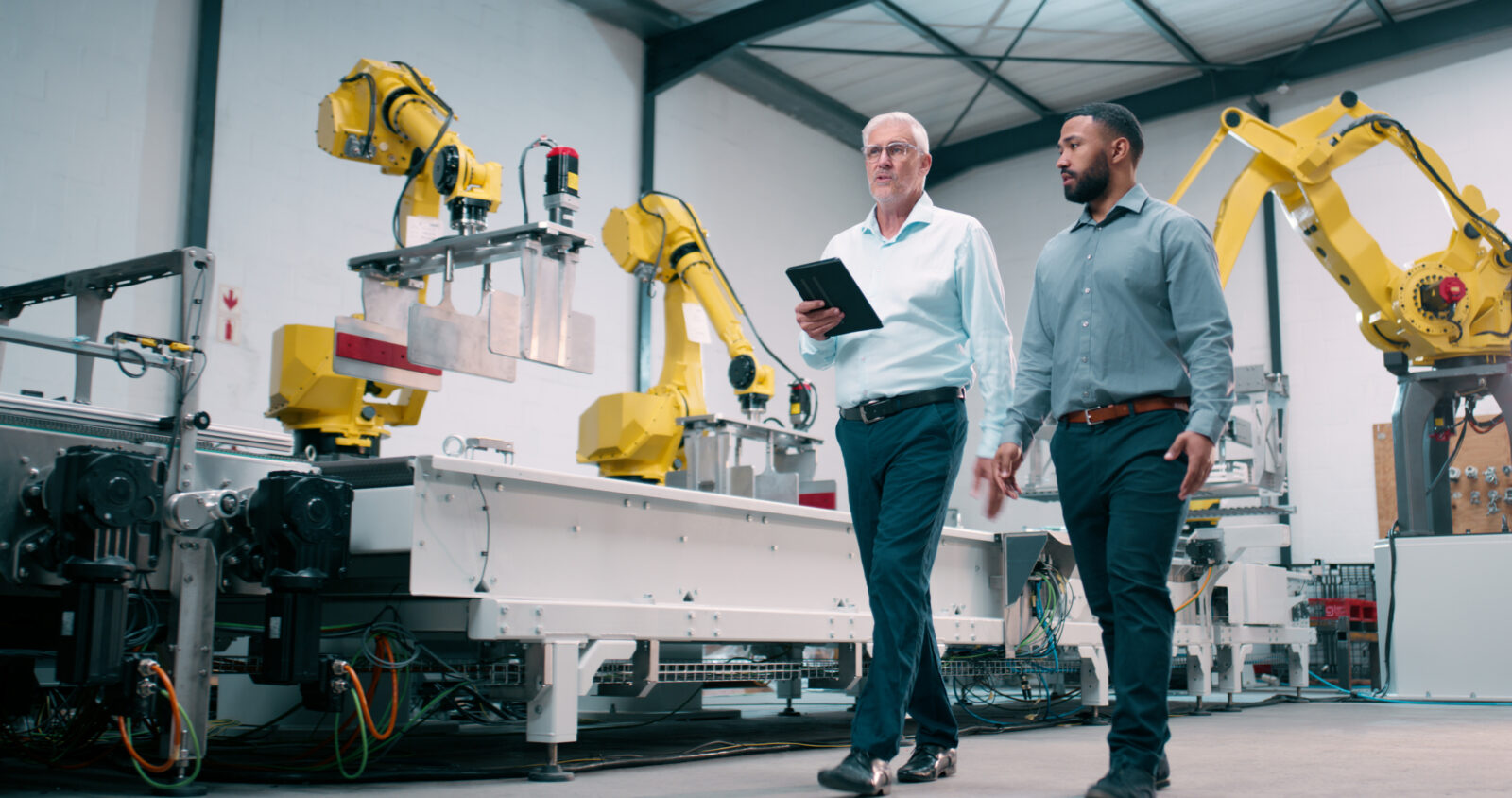 two people walking next to robot manufacturing arms